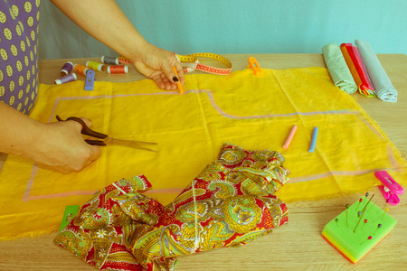 Close up of  woman's hands drawing a pattern on yellow tissue. Measuring tape and sewing...