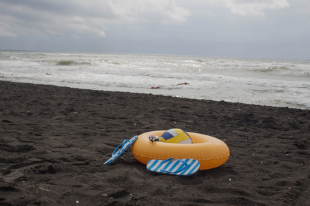 Ball, swimming glasses, sandal, and Floating Ring on beach. In the summer vacation. Beach life, overcastの写真素材