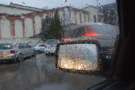 Blurry car silhouette seen through water drops on the car windshield. Drops Of Rain On Glass Backgroundの写真素材