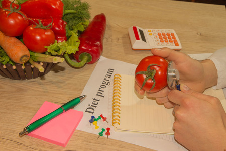 Young female nutritionist working in her office. Dietitian nutritionist checking examine a tomato with stethoscopeの写真素材