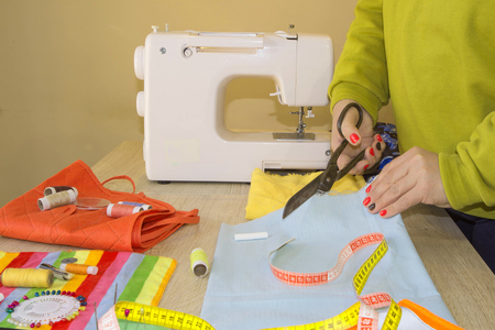 Couturier sews a dress in the studio. Fashion designer making a pattern on a red piece of tissue. Sewing machine is standing on the table beside themの写真素材