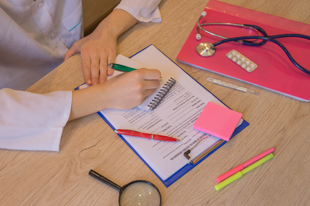 Female doctor with stethoscope sitting at a desk, writing something, prescription or recommendation of the patient, the photo. Concept photo doctorの写真素材