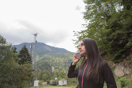 Young girl talking on phone next to an antenna of telecommunication.The concept of communication technology for smartphones and mobile phoneの写真素材
