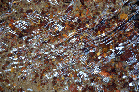 Zigzag and criss cross reflections and ripples on the water's surface of a pebble filled creek bedの写真素材