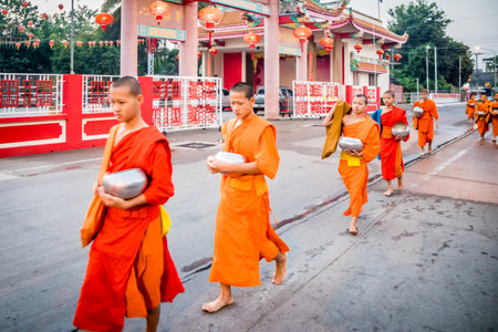 Mae Sot, Thailand - 3rd February 2019:   Young monks walking in a line past Chinese temple. Monks collect alms every morning.のeditorial素材