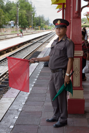 Hua Hin, Thailand - July 13th 2010: Stationmaster holding up a red flag to stop a train coming into Hua Hin railway station. The station is on the main line between Bangkok and the south of Thailandのeditorial素材