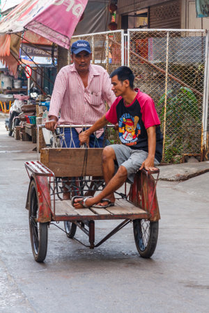 Mae Sot, Thailand - November 20th 2011: Man riding cart down street. The town is close to the Burmese border.のeditorial素材