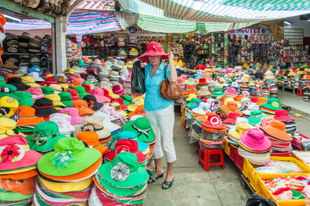 Ho Chi Minh City, Vietnam - February 24th 2010: A woman tourists tries on a hat in Cholon market. The market is one of the citys largest.のeditorial素材