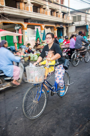 Mae Sot, Thailand - February 3rd 2019: Woman and child cycling through the morning market. Bicycles are widely used in the town.のeditorial素材