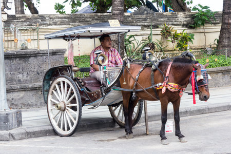 Bali, Indonesia - 3rd June 2017: Horse and carriage and driver waiting for customers, Kuta Beach....