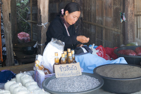 Chiang Rai, Thailand - December 10th 2014: Woman vendor selling rice and sewing at a roadside hill tribe market. The market sells handicrafts and food.のeditorial素材