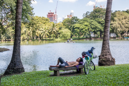 Bangkok, Thailand - 27th September 2018: Man with bike takes a rest by Lumphini Park lake. The park is in the centre of the city.のeditorial素材