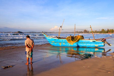 Mirissa, Sri Lanka - Decmber 30th 2016: Man stood by a traditional fishing boat ashore. The boats return early morning after a nights fishing.のeditorial素材