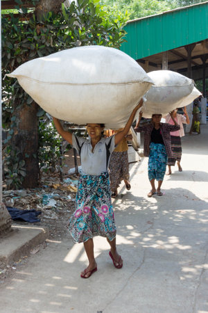 Yangon, Myanmar - May 5th 2014: Women carrying large sacks on their heads. It s common to see women carrying loads in this way.のeditorial素材