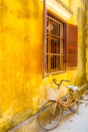 Bicycle leaning up against a yellow wall with window and shuttersの写真素材