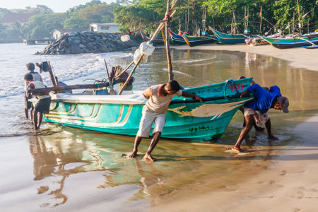 Galle, Sri Lanka - March 14th 2011:  Fishermen dragging a boat up on to the beach. The beach is also used as a fish market.のeditorial素材