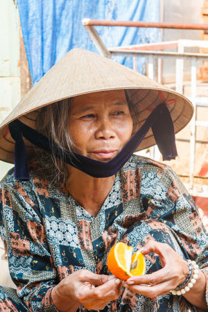 Hoi An, Vietnam - March 3rd 2010: Woman cutting up an orange on a market. Markets are held every day.のeditorial素材
