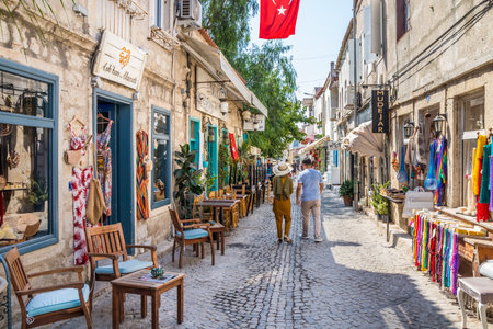 Alacati, Turkey - September 4th 2019: Couple walking down a narrow street with shops. The town is a...