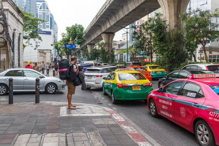Bangkok, Thailand - 23rd March 2018: A backpacker waits for an empty taxi in heavy traffic on Sukhumvit Road. Taxis are difficult to find at peak times.のeditorial素材