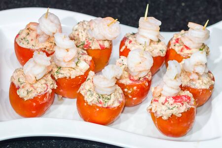 Tomatoes stuffed with crab meat and prawns on a white plateの写真素材