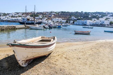 Small boat beached on sand with Mykonos harbour, Greece in the backgroundの写真素材