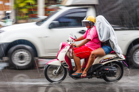 Phuket, Thailand - June 25th 2010: Motorcyclist and passenger in the rain. The monsoon season brings very heavy rains.のeditorial素材