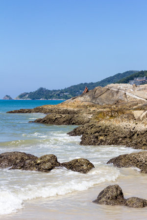 Phuket, Thailand - 11th December 2017: Man sat on rocks at north end of Patong Beech. This is a relatively quiet part of the beach.のeditorial素材