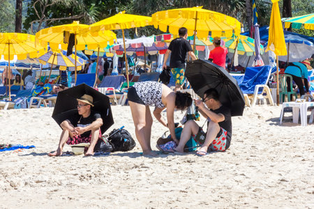 Phuket, Thailand - 11th December 2017: Asian tourists with black umbrellas on Patong beach. Many tourists come from all over the world.のeditorial素材