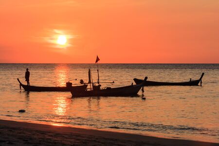 Fisherman silhouetted on his boat at sunset, Nai Yang beach, Phuket, Thailandの写真素材