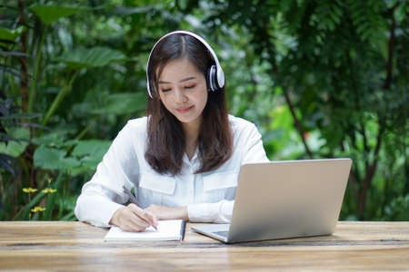 Young female student with headphone sit by laptop choose course online at distance learning web platform of university. woman work or study from home using modern technologyの写真素材