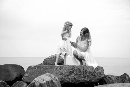 black and white photo, mother and daughter dancing on big rocks, on a wild beach near the sea