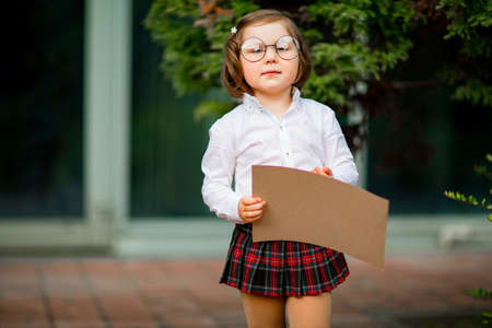 a girl in a school uniform stands near the school, with a piece of paper, a layout with space for textの写真素材