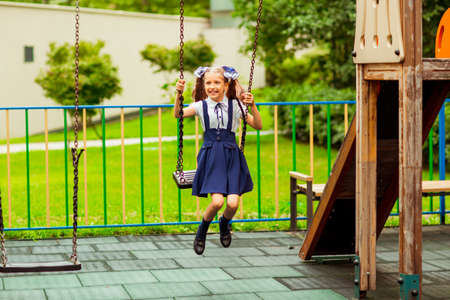 schoolgirl in school uniform, swinging on a swing in a children's amusement Parkの写真素材