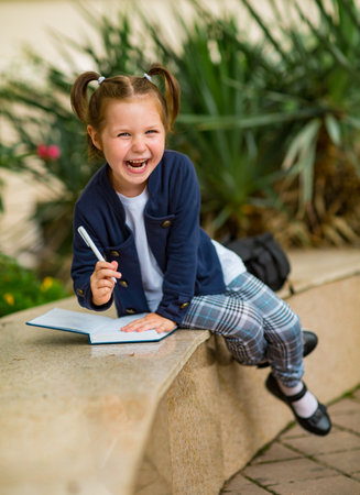 a beautiful little girl, a schoolgirl, in the afternoon near the school, in a school uniform with two ponytailsの写真素材
