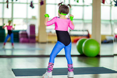 a small, beautiful girl, doing fitness in the gym, in bright, colored sportswearの写真素材