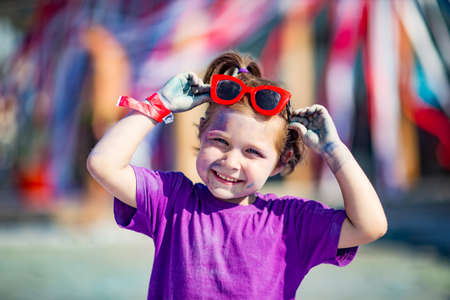 a little, cheerful girl at the Holi festival, in a purple T-shirt, stained with lilac paintの写真素材