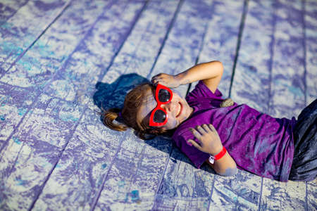 a little, cheerful girl at the Holi festival, in a purple T-shirt, stained with lilac paintの写真素材