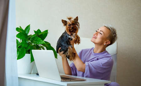 a young, beautiful woman, blonde,is sitting next to a laptop, in purple pajamas, and holding a small...