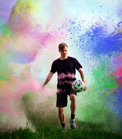 A handsome young man, a football player, in a black uniform, with a soccer ball on the street in holly colorsの写真素材