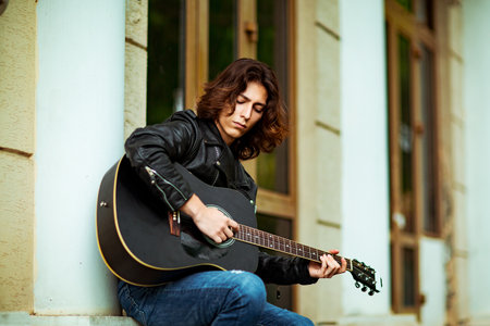Young man with guitar sitting on the street and looking at the camera