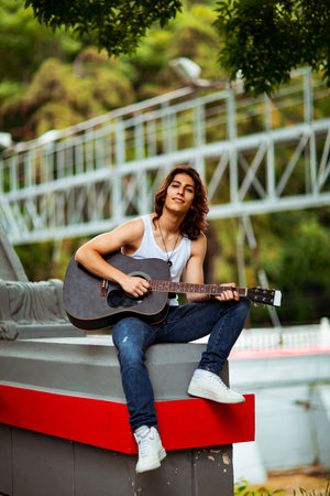A young, handsome man with long, dark hair, playing an acoustic guitar, on the streets of the city, in a white T-shirt and jeansの写真素材