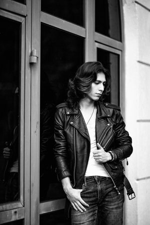 Black and white photo of a young man with long hair, wearing a leather jacket and jeans and a white T-shirtの写真素材