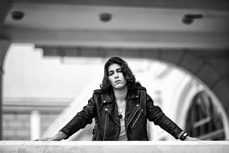 Black and white photo of a young man with long hair, wearing a leather jacket and jeans and a white T-shirtの写真素材