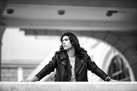Black and white photo of a young man with long hair, wearing a leather jacket and jeans and a white T-shirtの写真素材