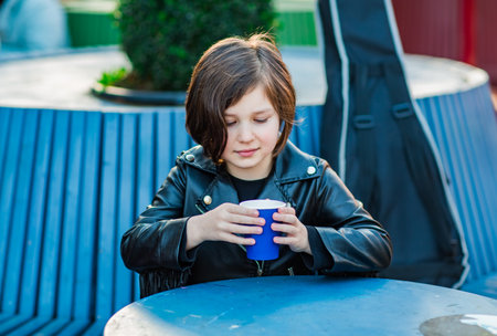 A girl with a square hairstyle, sitting in a summer cafe on a blue bench and drinking tea from a...