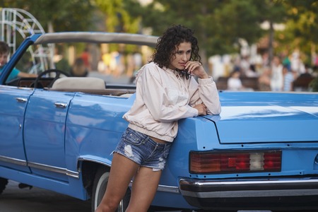 Beautiful curly girl in shorts and blue retro cabriolet