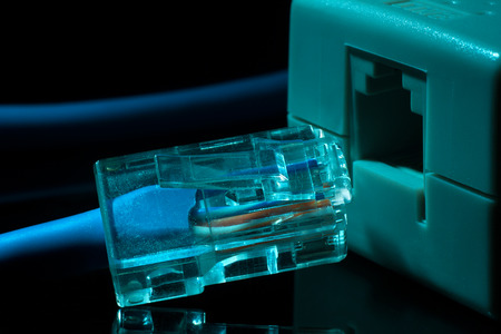 Twisted pair (patch cord) blue network Internet cable in blue tones on a black background is inserted into the network connectorの写真素材