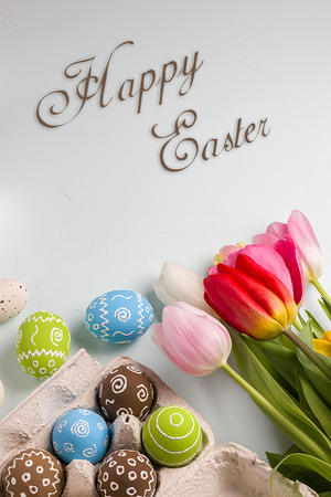 Painted easter eggs and bouquet of spring tulips closeup on a light blue background with space for congratulationの写真素材