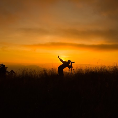 silhouette of photographer taking picture of landscape during sunsetの写真素材