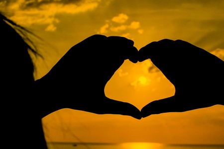 Heart shape making of hands against bright sea sunset and sunny golden way at waterの写真素材